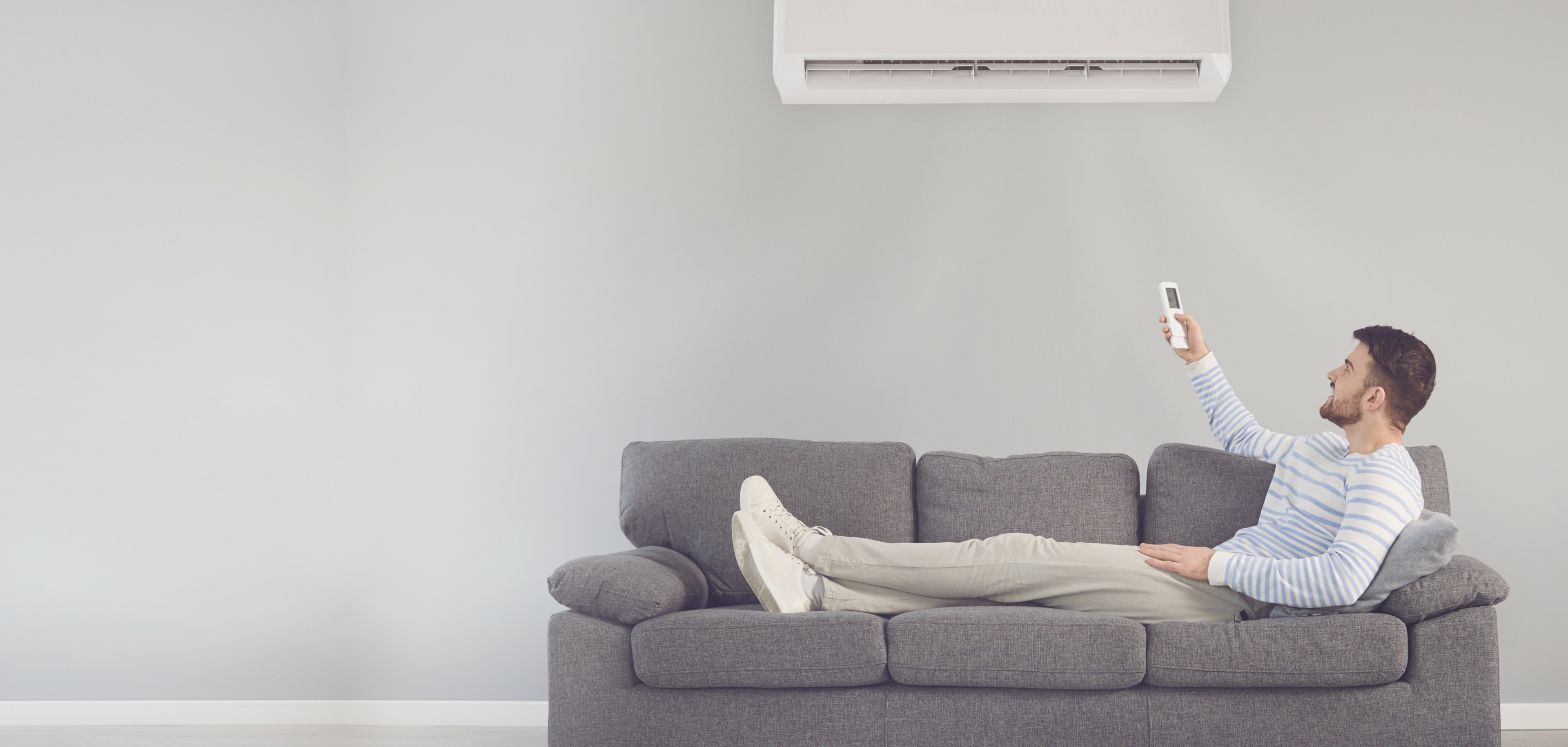 A person laying on the couch under an air conditioner.